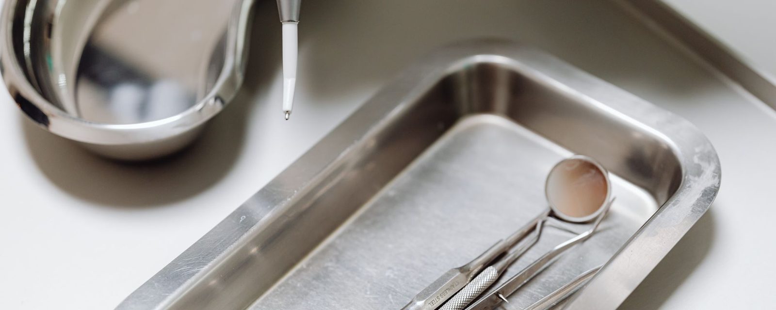 Steel dental instruments, a mirror and probe, laid out on a tray.