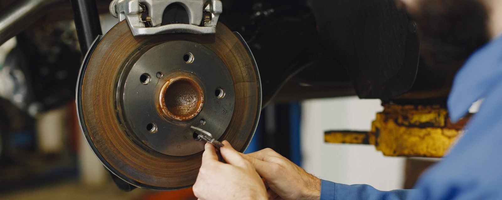 A mechanic's hands working on a car's brake disc and caliper in a garage workshop