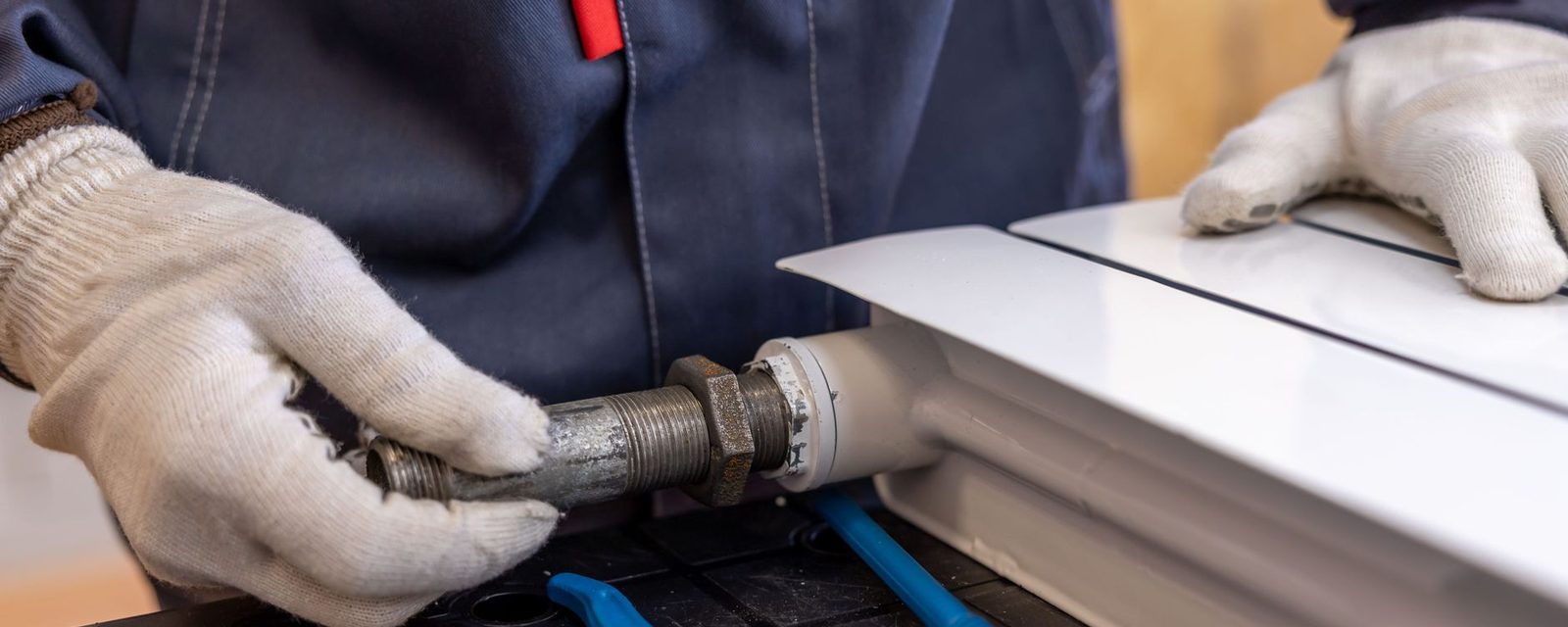A gloved hand fitting a valve onto a white radiator.