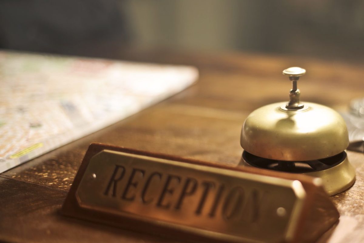 A brass reception bell and desk plate on a wooden desk.