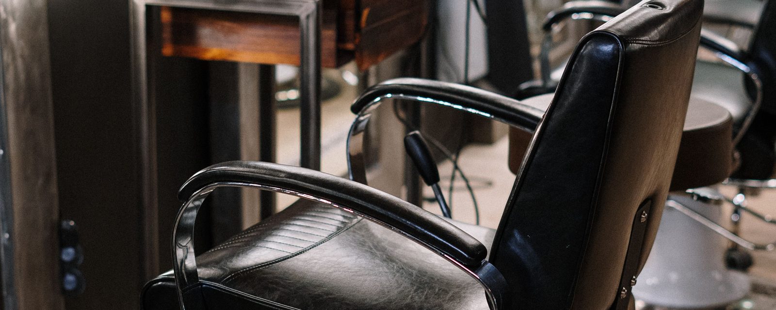 A black leather salon chair with chrome arms in front of an illuminated mirror