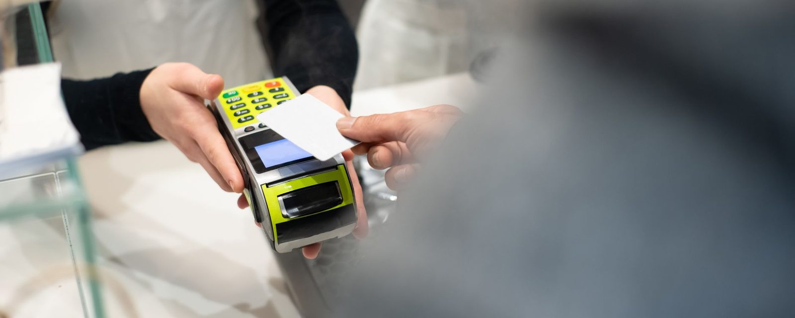 A customer's hand tapping a bank card on a card machine held across a shop counter
