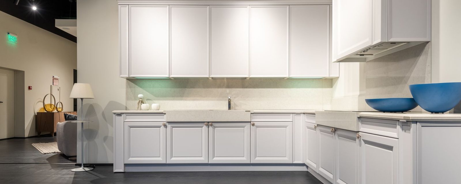 White fitted kitchen units with a stone-effect worktop on a showroom floor