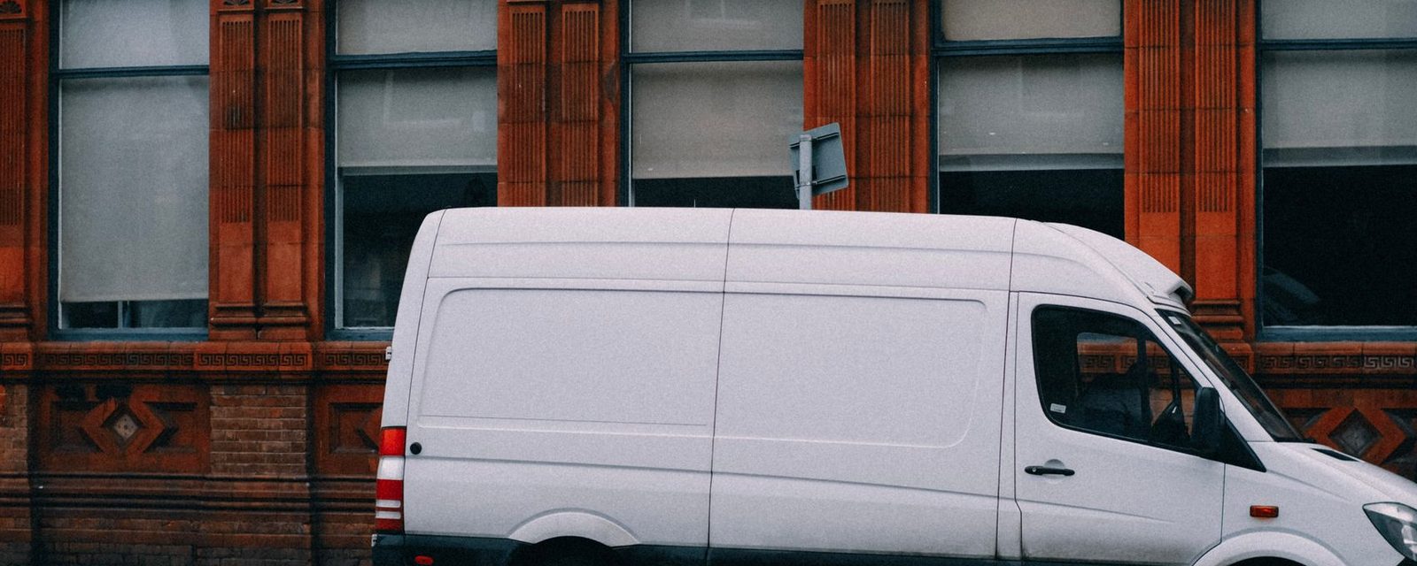 A plain white panel van parked against a red-brick building.