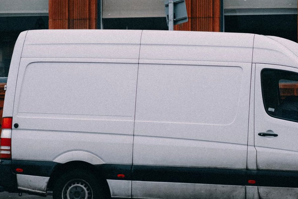 A plain white panel van parked against a red-brick building.