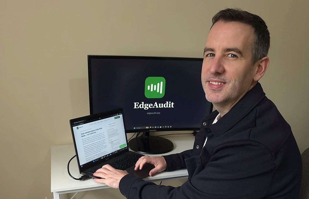 Stephen McLaughlin at his desk in Derry, working on the EdgeAudit site, with the EdgeAudit logo on the monitor behind him